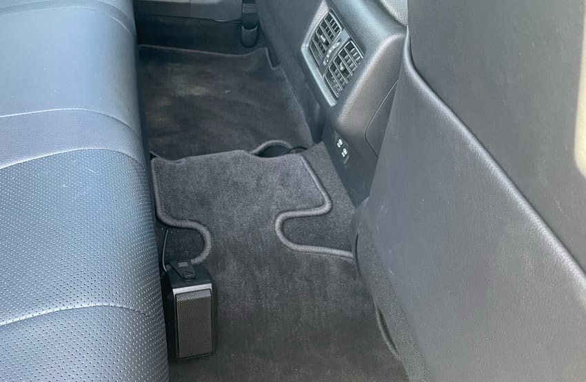 A black speaker in the rear passenger foot area on the side of the raised center area.