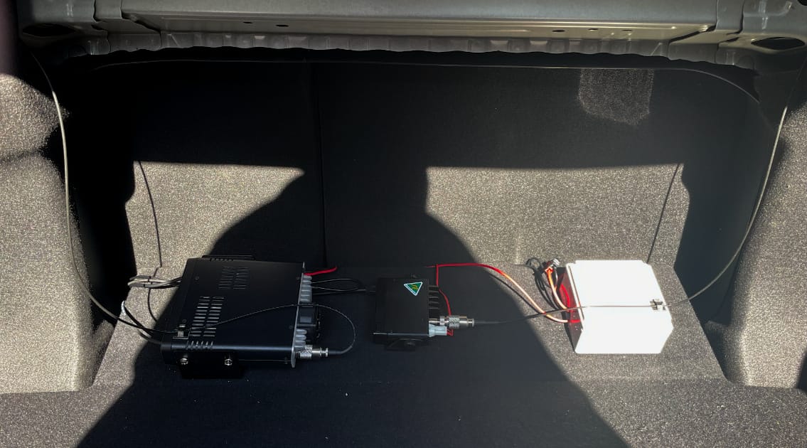 The most forward section of the boot in a 2019 Toyota Camry. There are three devices mounted to the floor panel with some cables connecting them up to each-other and other components. From left to right they are a large black main unit of the ICOM 2730A, the small main unit of the GME XRS-330C, and a white enclosure from Jaycar that houses the relay.